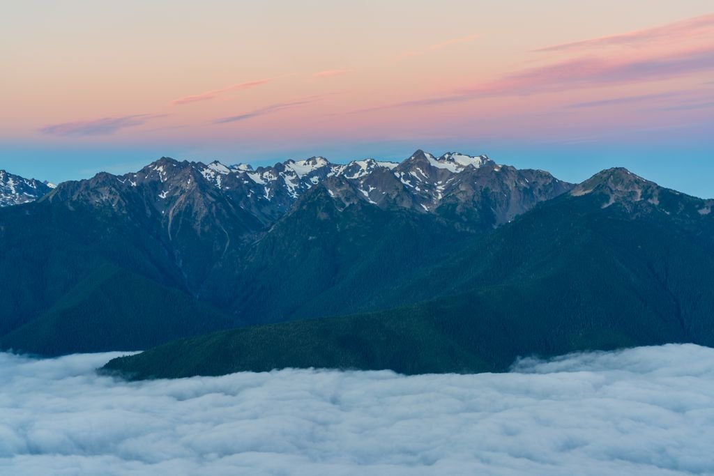 Aerial view of snow capped mountain peaks above clouds at sunrise, showcasing dramatic sky and serene nature.