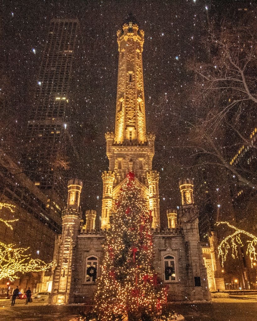 Night view of a historic water tower adorned with festive lights and a Christmas tree, creating a magical holiday ambiance.