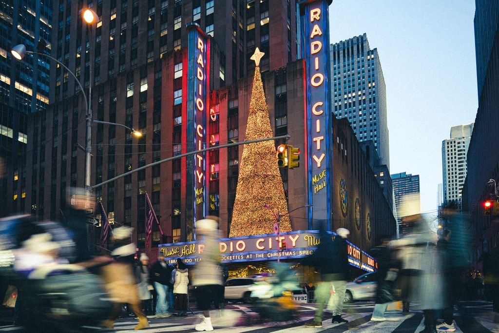 Radio City Music Hall decorated for Christmas in New York City with a lit Christmas tree and bustling crowds.