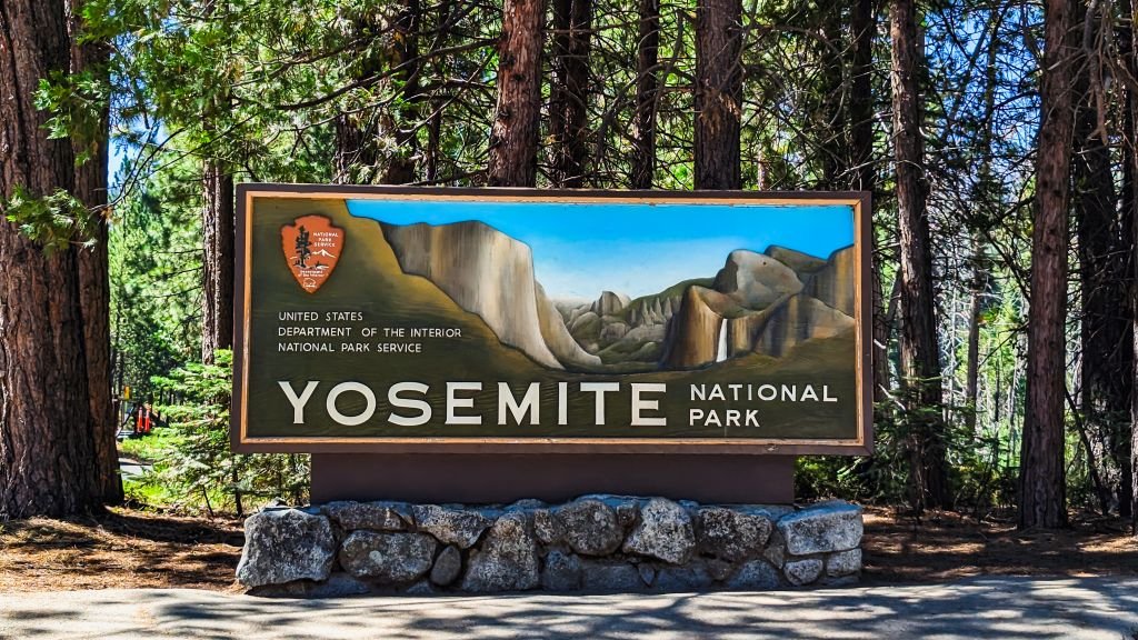 Yosemite National Park entrance sign set against a backdrop of towering trees.