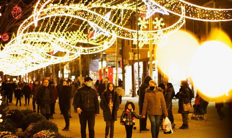 Street at night strung with Christmas lights, crowds walking