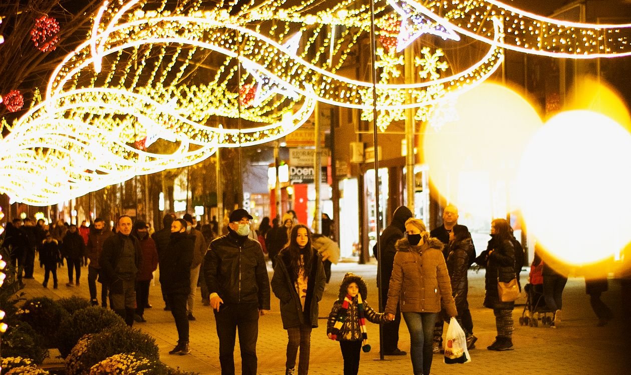 Street at night strung with Christmas lights, crowds walking beneath glowing overhead displays